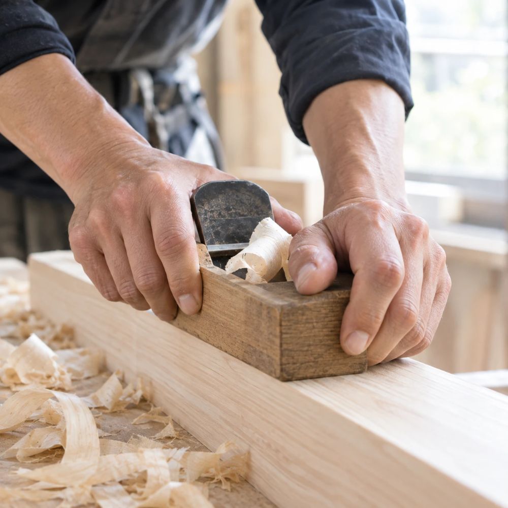 かんなを手前に引いて木材を削る大工の手元